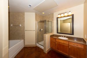 Apartments in Uptown Houston, Galleria Area A modern bathroom in a three-bedroom apartment featuring a bathtub on the left, a glass-enclosed shower in the center, a vanity with sink and mirror on the right, and elegant brown tile flooring. The Augusta Apartments In The Galleria Area of Houston 2660 Augusta Drive Houston, TX 77057 p: (832) 648-3088 f: (832) 675-0401